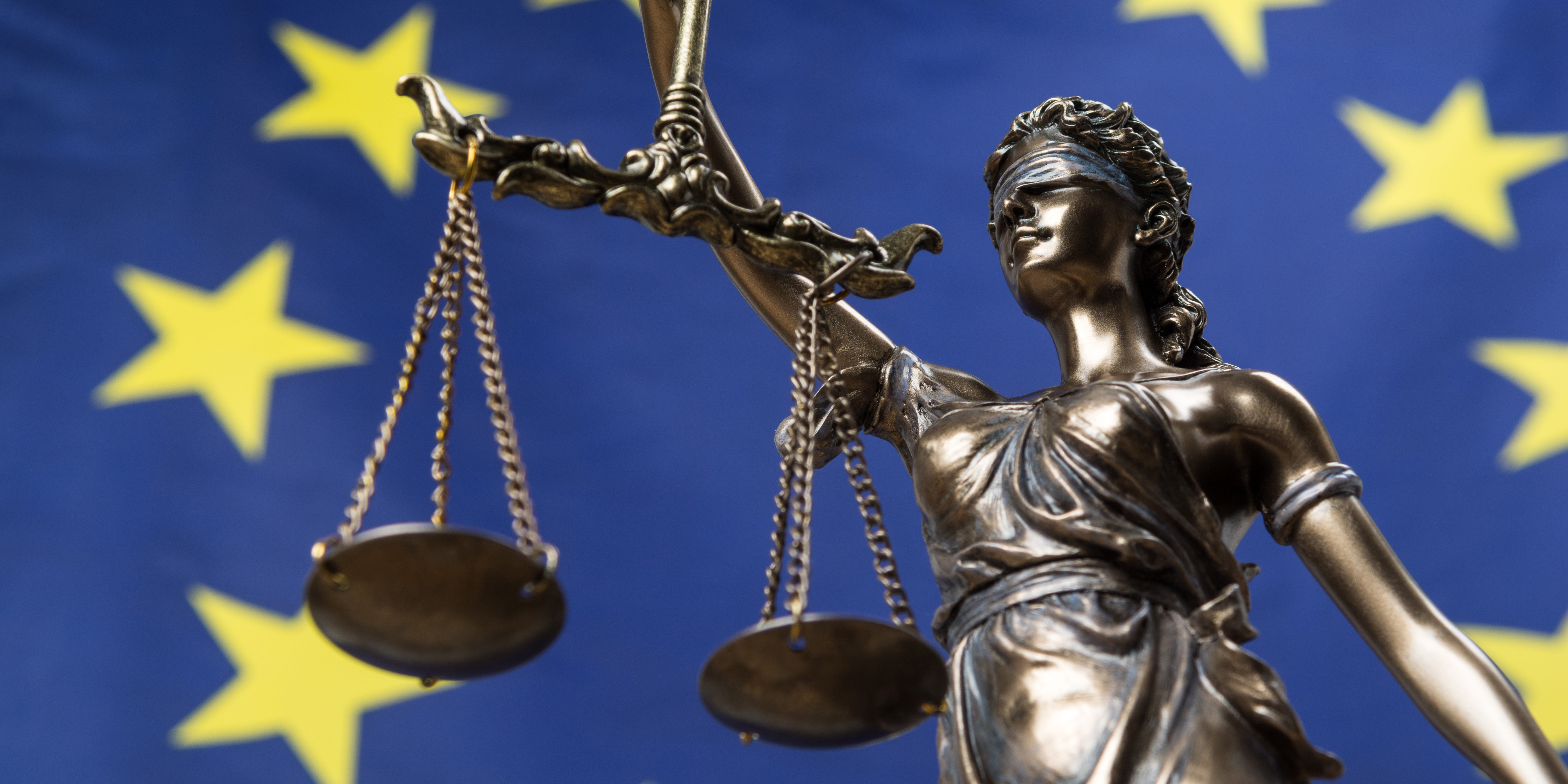 Statue of the blindfolded goddess of justice Themis or Justitia, against an European flag, as a legal concept