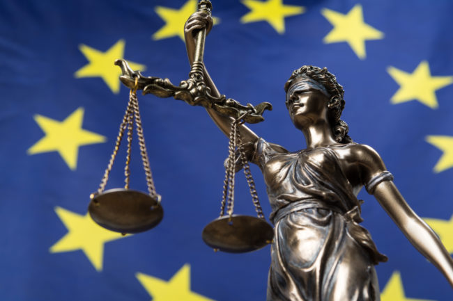 Statue of the blindfolded goddess of justice Themis or Justitia, against an European flag, as a legal concept